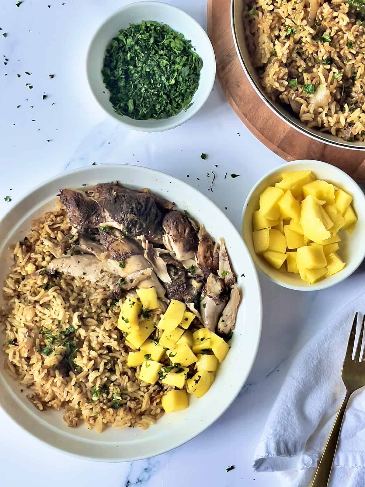 instant pot jerk chicken and rice in a white bowl with a bowl of cilantro and bowl of mango, next to a large serving dish or Carribean rice.