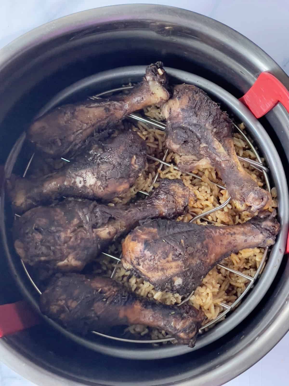 Jamaican jerk chicken drum sticks on a tivet on top of a pan of rice in the pressure cooker