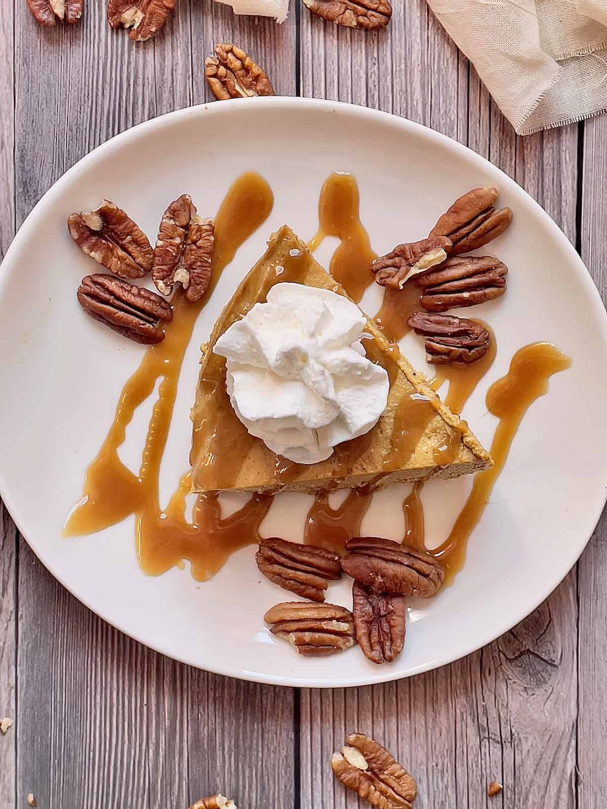 instant pot pumpkin cheesecake on a white plate topped with pecans and caramel sauce