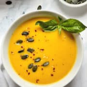 instant pot pumpkin soup topped with pepitas, red pepper and basil in a white bowl