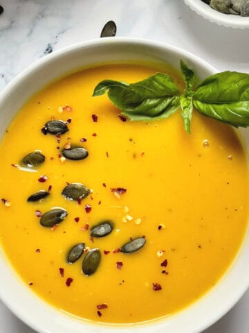 instant pot pumpkin soup topped with pepitas, red pepper and basil in a white bowl