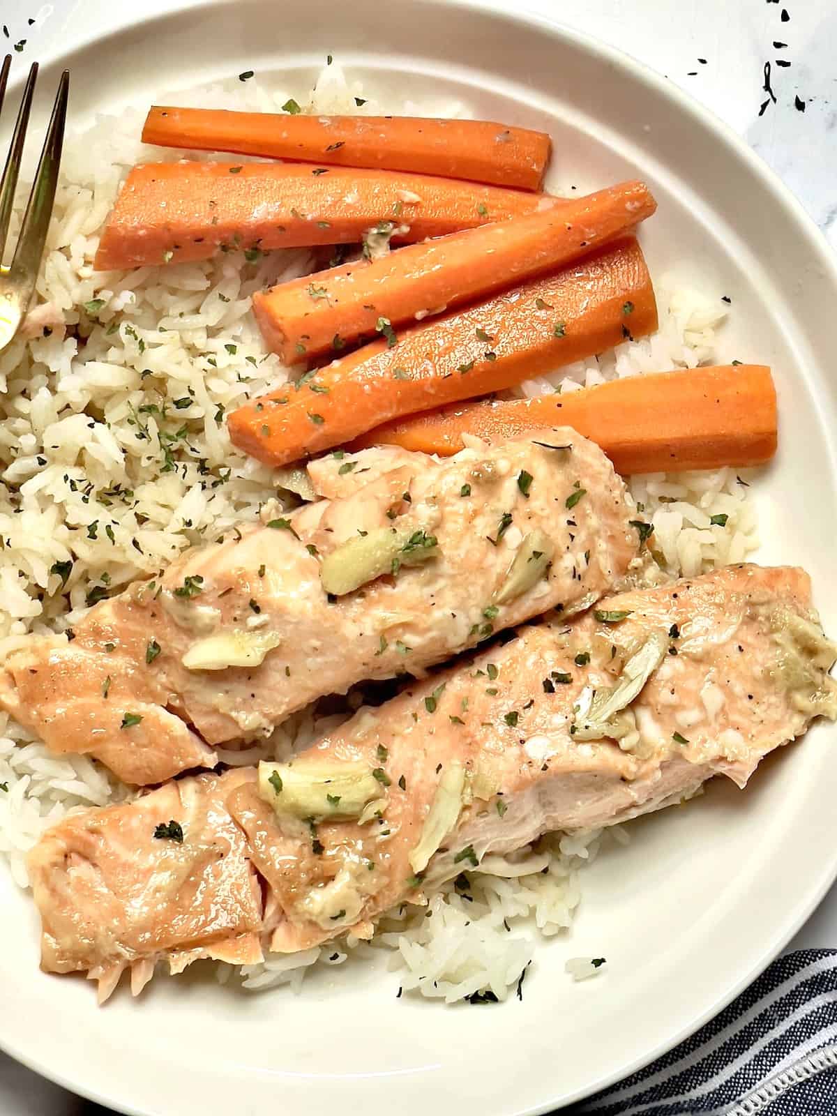 salmon, carrots, and white rice topped with parsley in a white plate