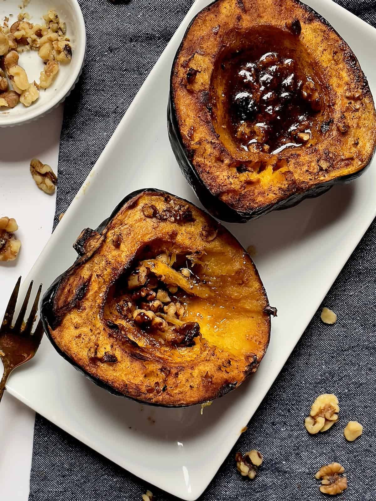 roasted acorn squash with walnuts and honey butter on a white plate