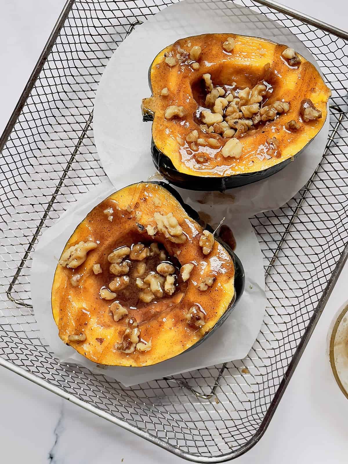 acorn squash in an air fryer basket topped with walnuts and honey butter sauce