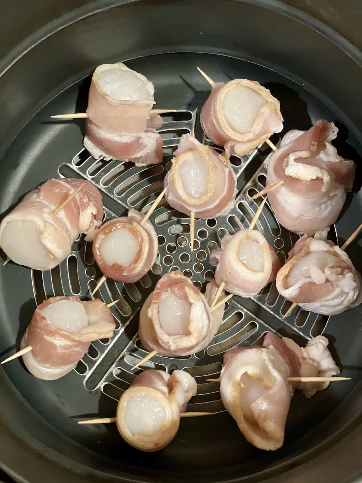 raw scallops wrapped in bacon in an air fryer basket