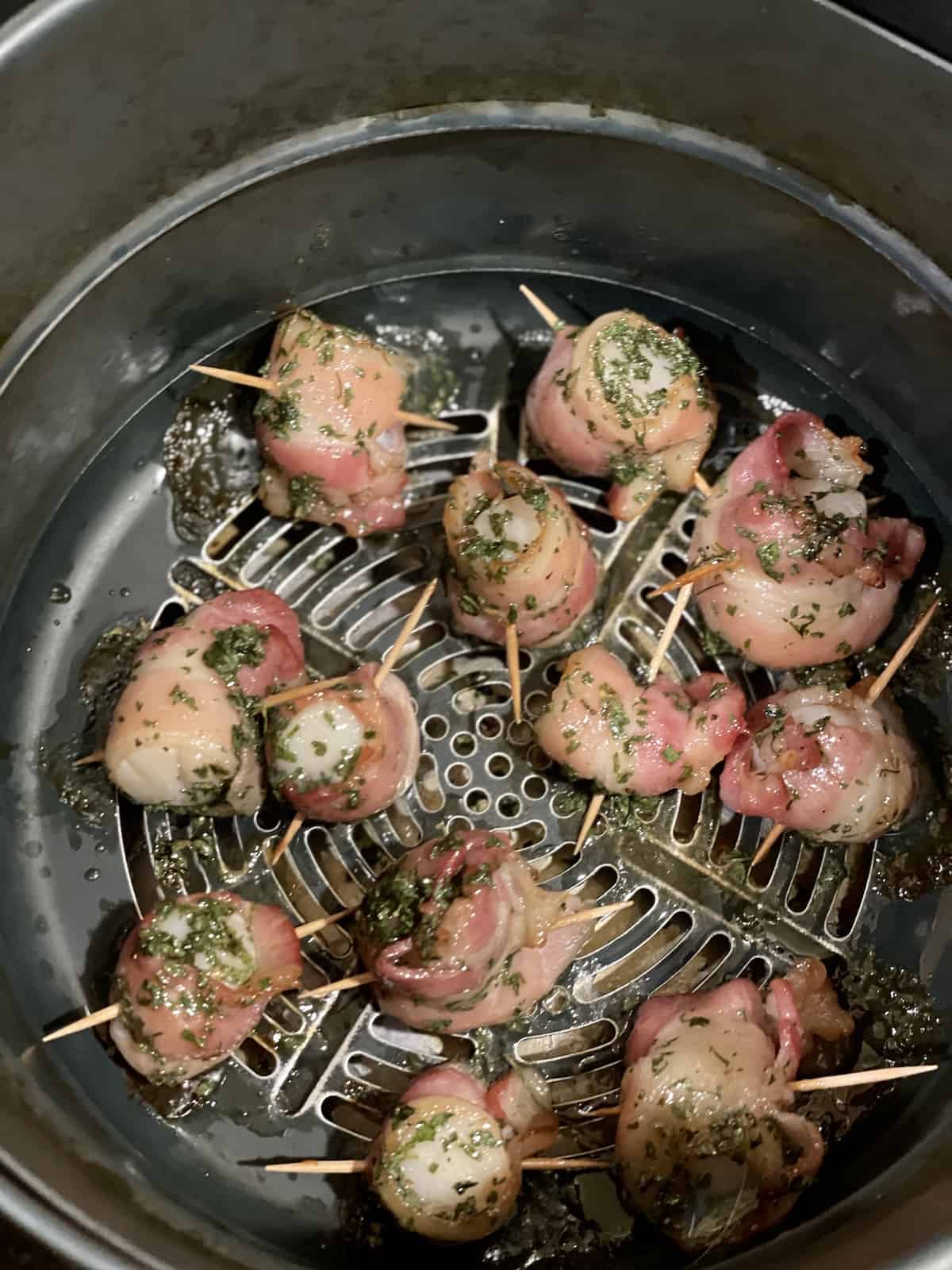 raw scallops wrapped in bacon in an air fryer basket topped with maple syrup glaze