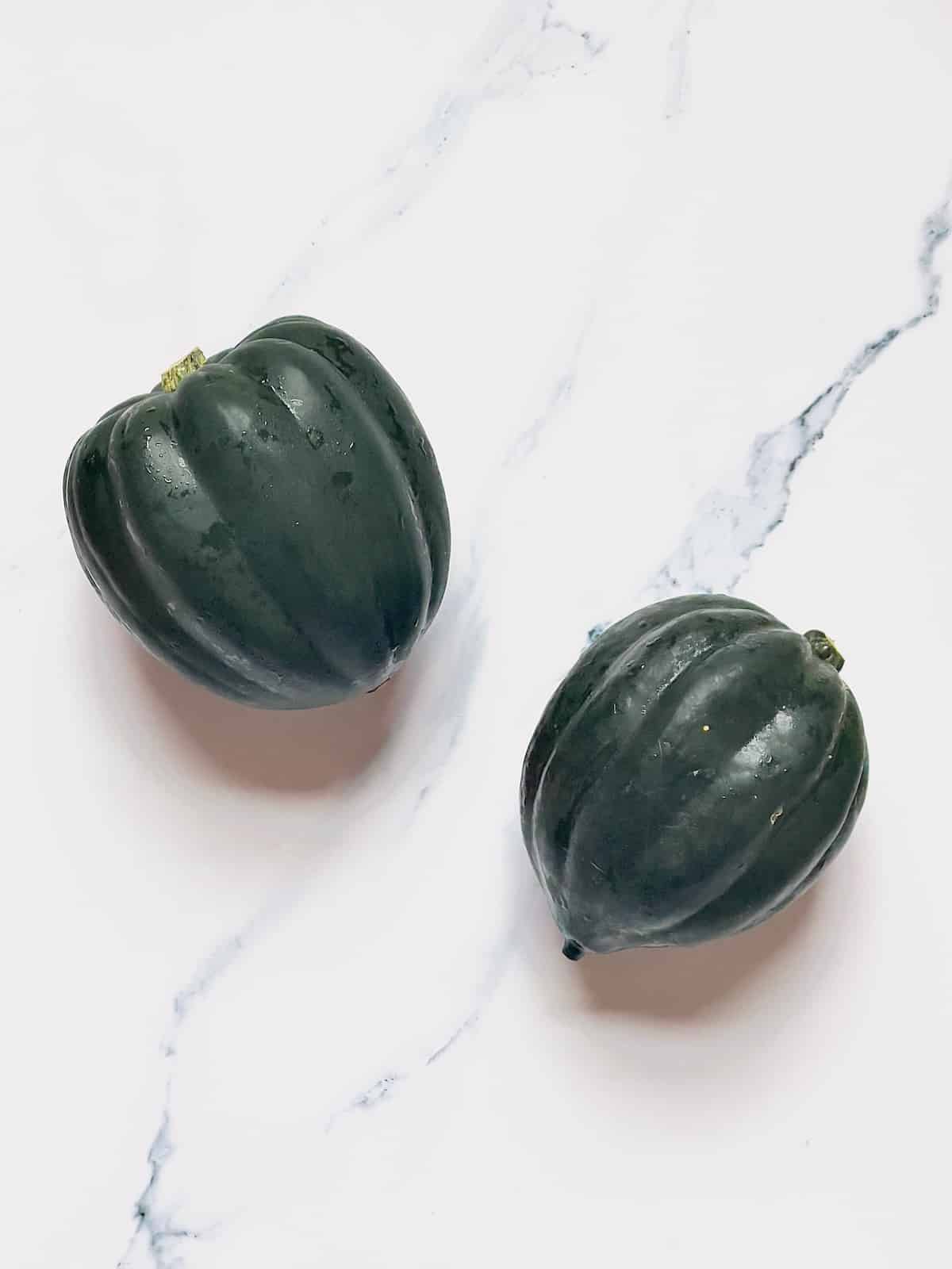 two dark green acorn squash on a white board