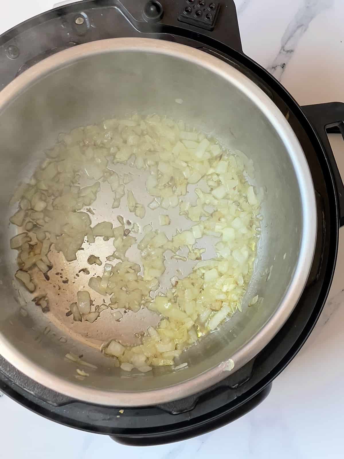 onions and garlic sauteing in a pressure cooker