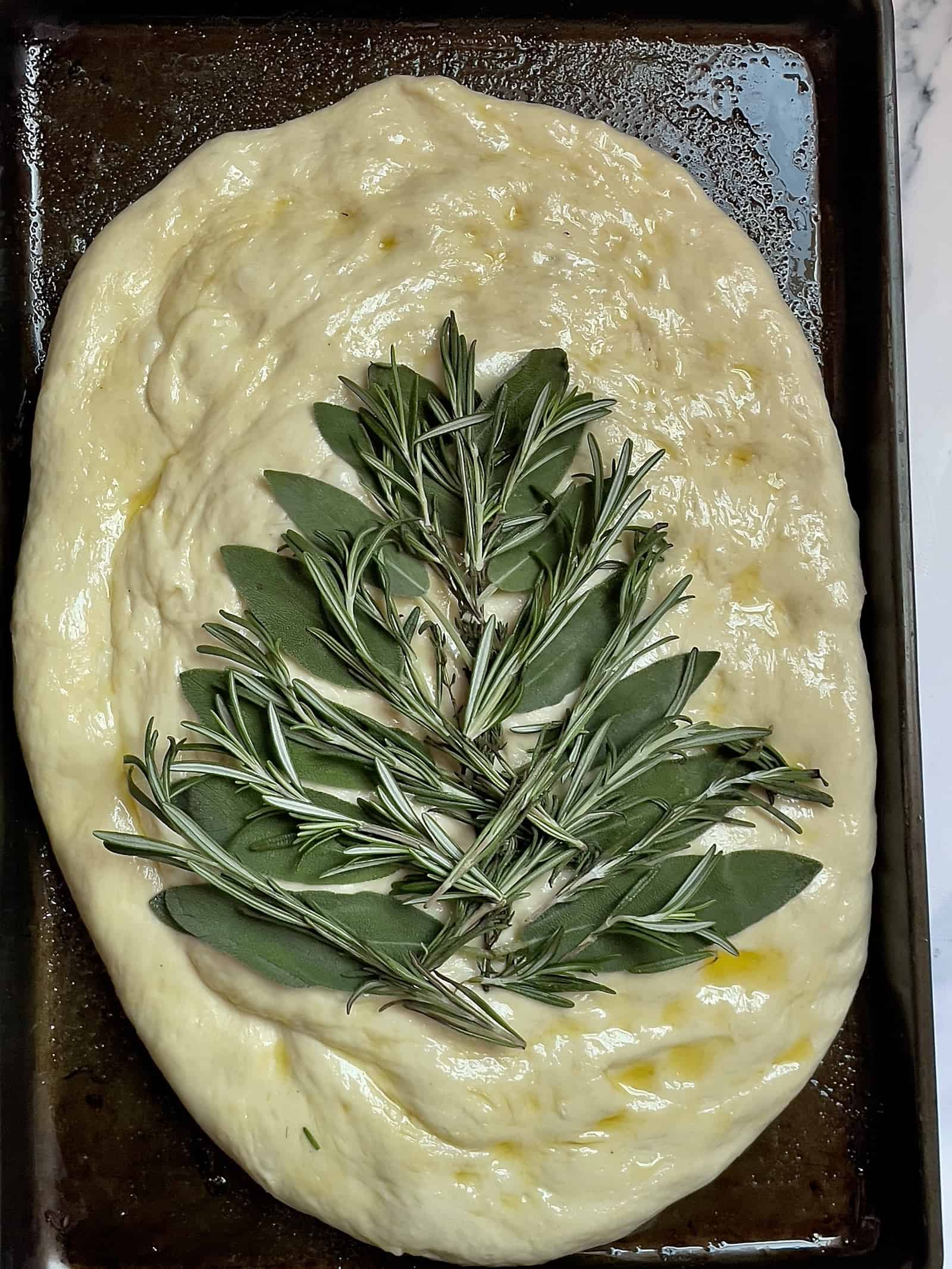 sage leaves and rosemary spread out around a piece of thyme on focaccia bread