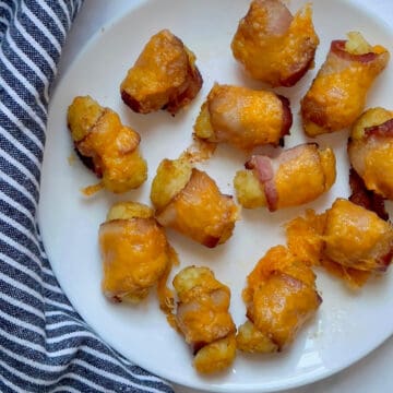 air fried tater tots wrapped in bacon and topped with cheddar cheese on a white plate