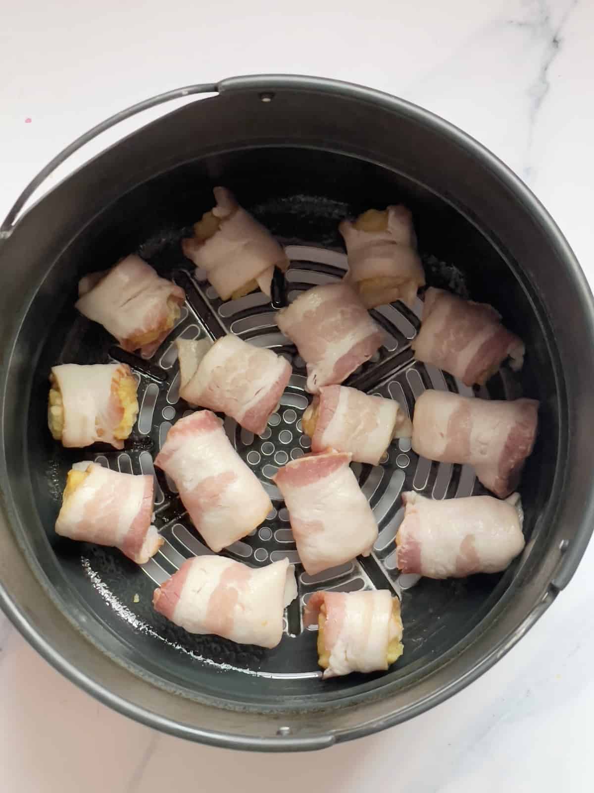 uncooked bacon wrapped tater tots in an air fryer basket