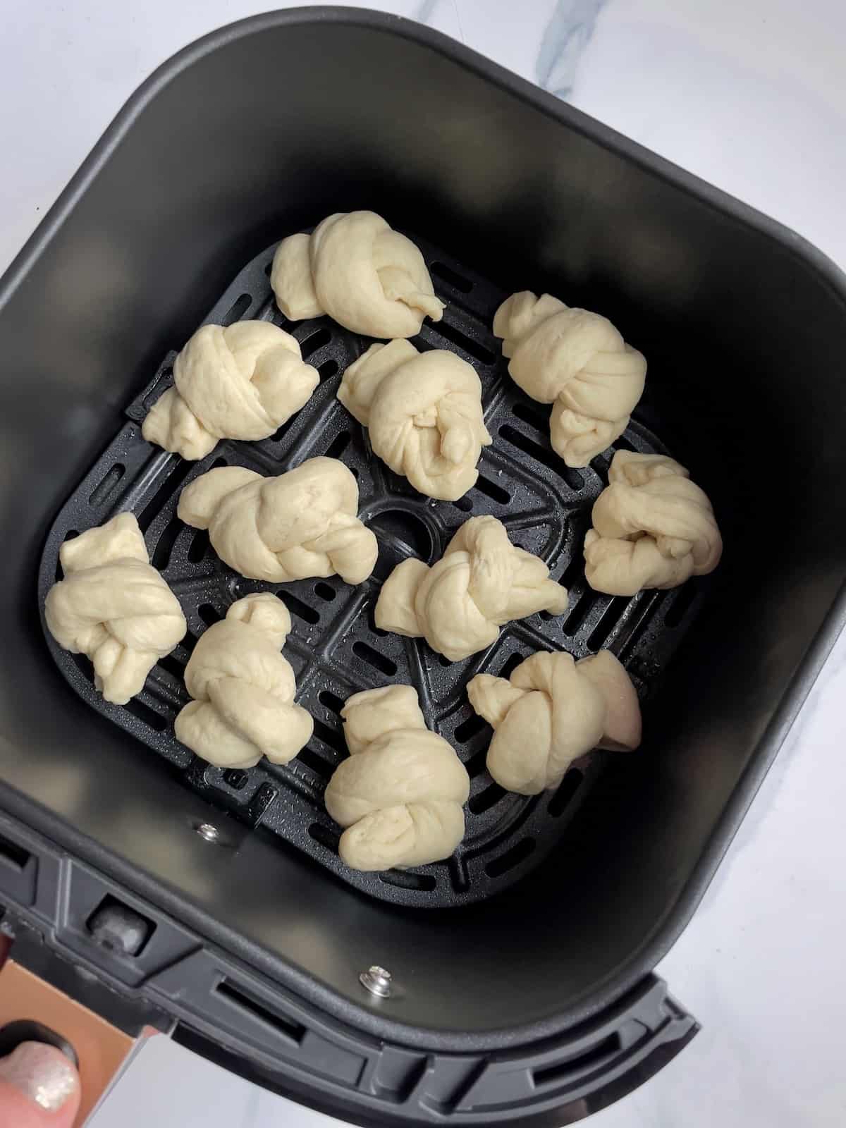 garlic knots in an air fryer basket, uncoked
