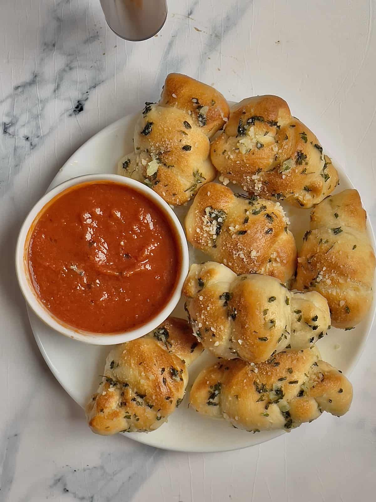 garlic knots on a white plate sprinkled with parmesan cheese