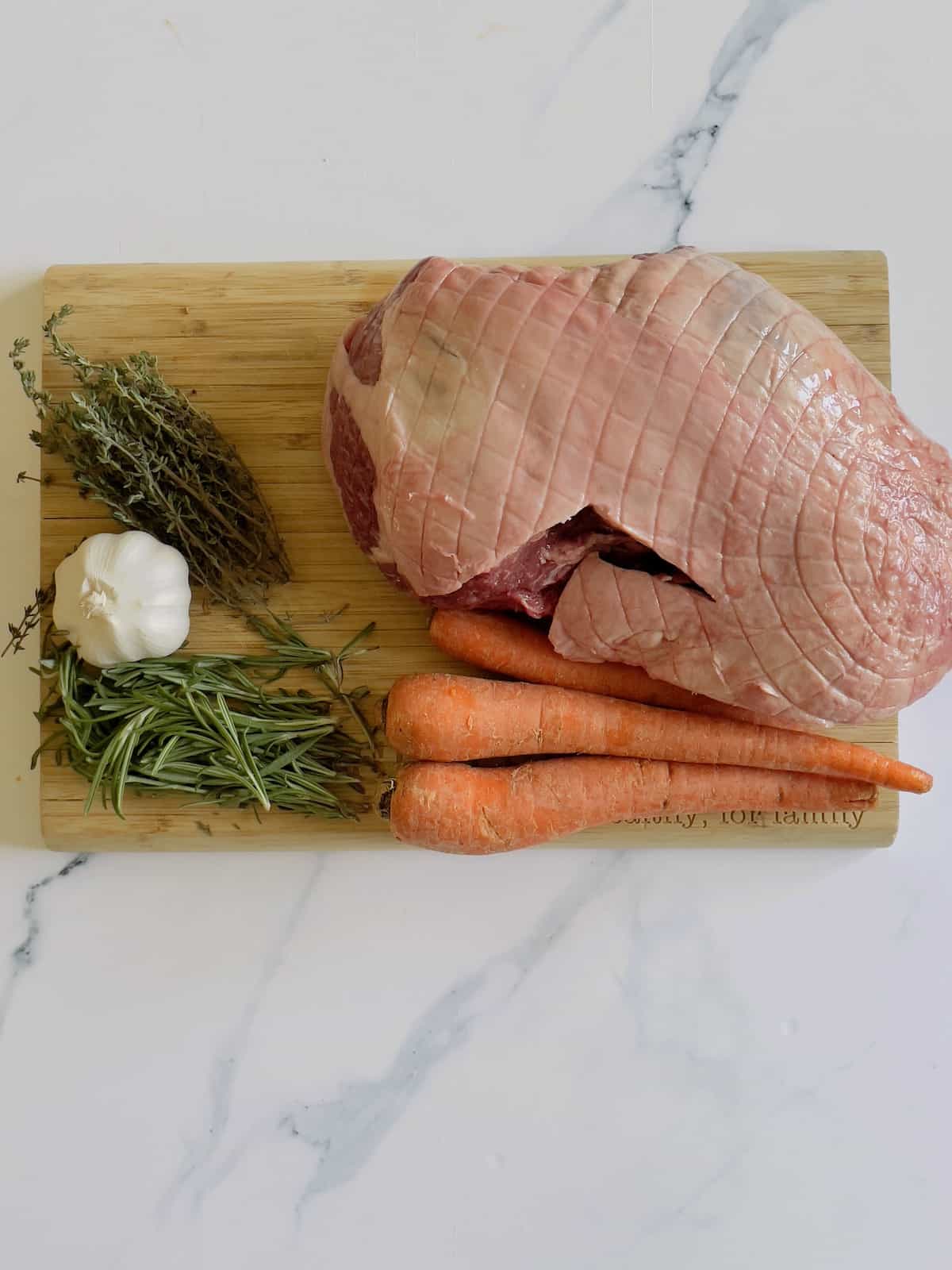lamb roast, carrots, garlic, and fresh herbs on a cutting board