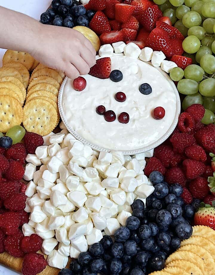child dipping a strawberry into fruit dip on a santa charcuterie board