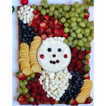 fruit, cheese, crackers on a wooden board in the shape of santa clause face