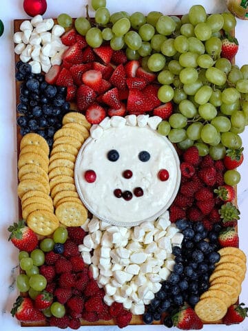 fruit, cheese, crackers on a wooden board in the shape of santa clause face