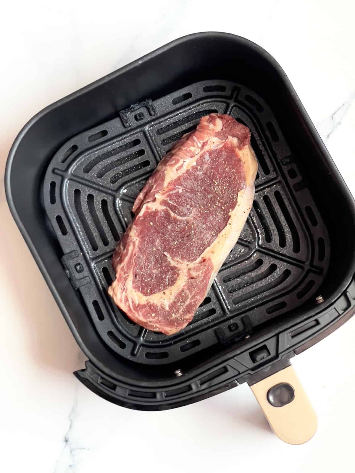 raw ribeye steak in an air fryer basket