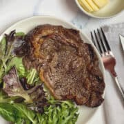 air fryer ribeye steak on a white plate with spring mix lettuce and butter