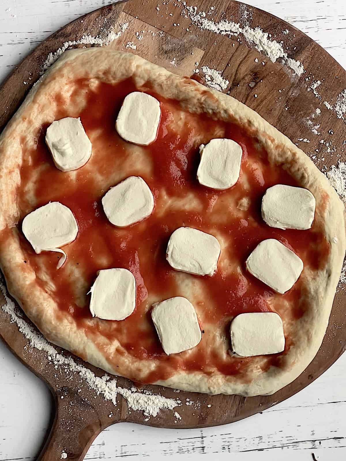 uncooked neapolitan pizza dough on a pizza peel, topped with sauce and mozzarella slices