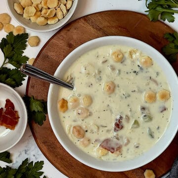 instant pot clam chowder new england style in a white bowl topped with oyster crackers and surrounded by parsley, oyster crackers and bacon