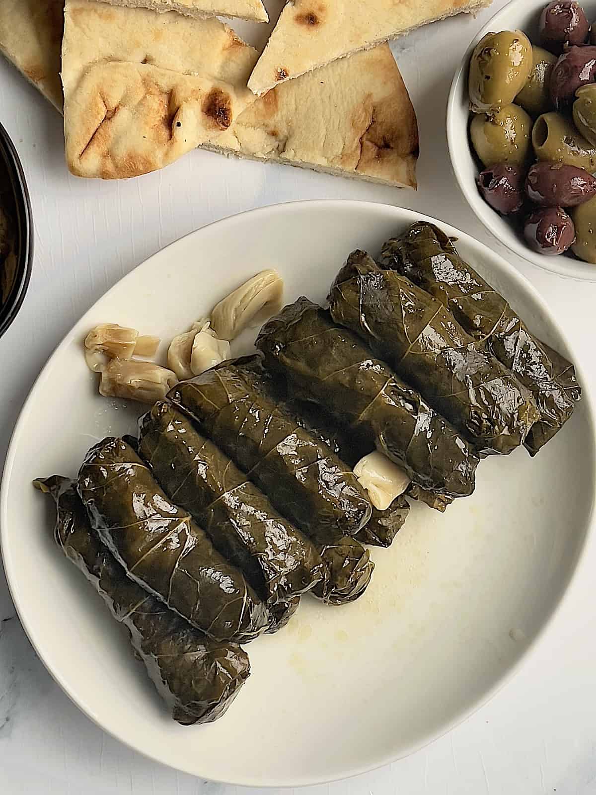 Instant pot grape leaves on a white plate surrounded by pita chips and olives