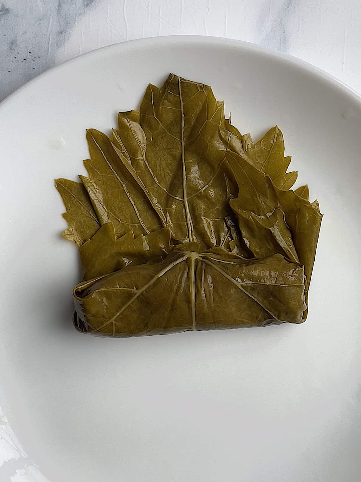 step 3 of how to roll a grape leaf, with the ends tucked in and under the stuffing
