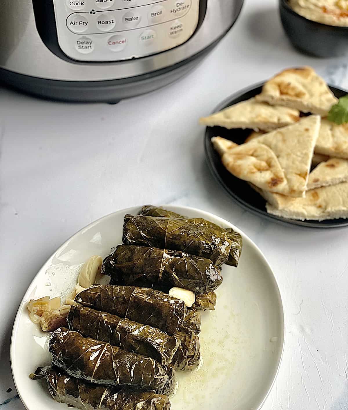 pressure cooked grape leaves on a white plate with an Instant Pot in the background