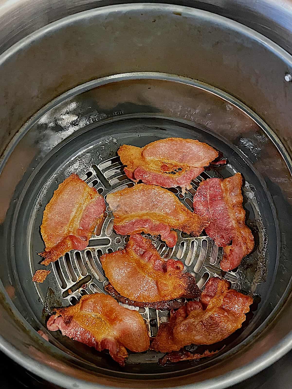 crispy bacon cooking in an air fryer basket