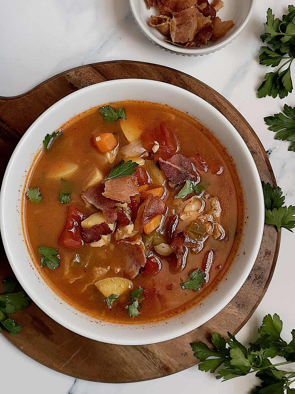 instant pot manhattan clam chowder soup in a white bowl surrounded by bacon and parsley