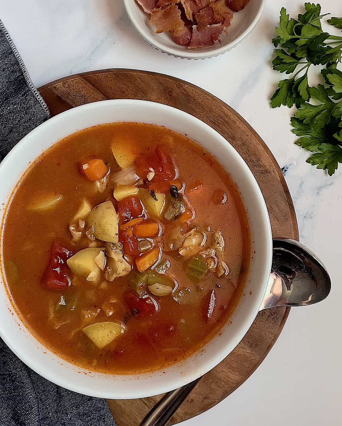 instant pot manhattan clam chowder soup in a white bowl surrounded by bacon and parsley