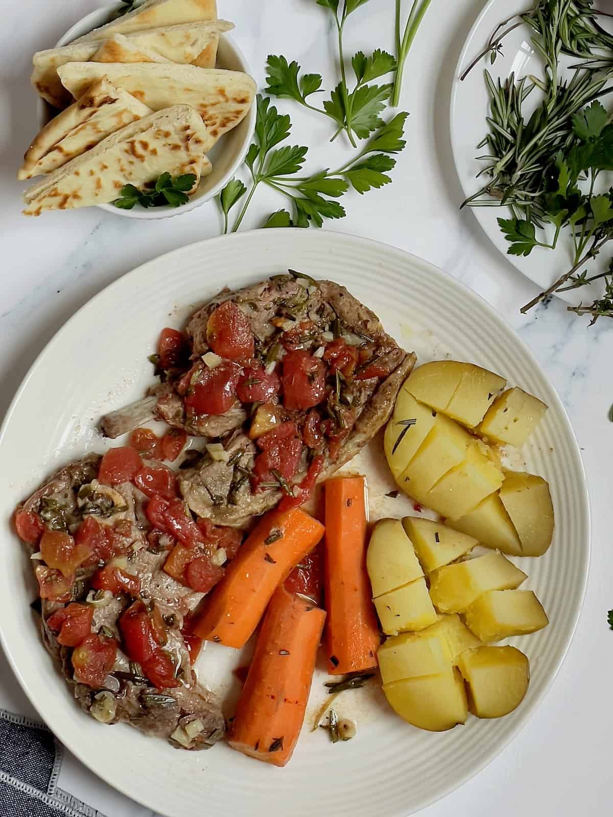 slow cooker lamb shoulder with carrots and potatoes on a white plate topped with tomato broth