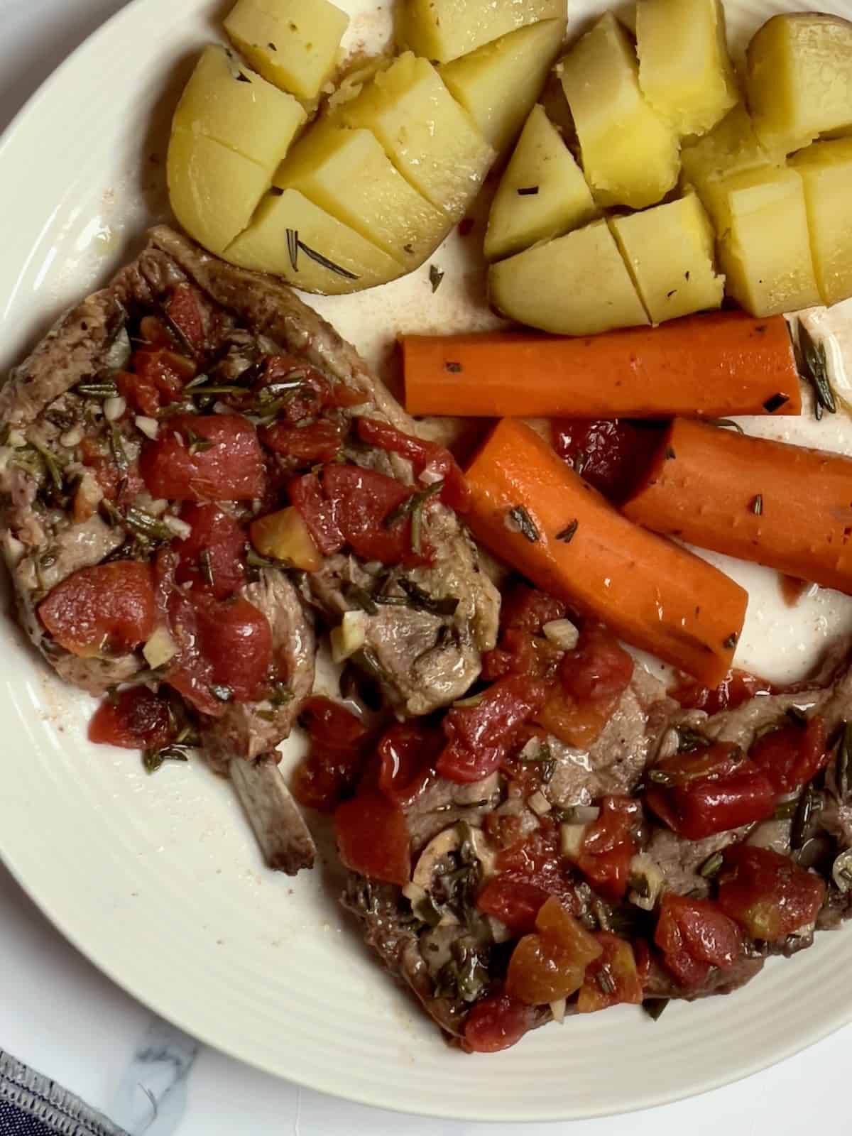 slow cooker lamb shoulder with carrots and potatoes on a white plate topped with tomato broth