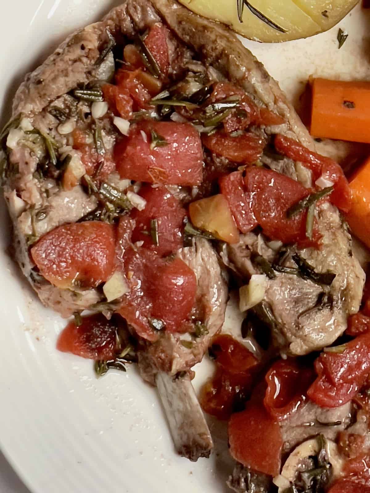 slow cooker lamb shoulder with carrots and potatoes on a white plate topped with tomato broth