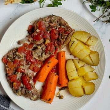 slow cooker lamb shoulder with carrots and potatoes on a white plate topped with tomato broth