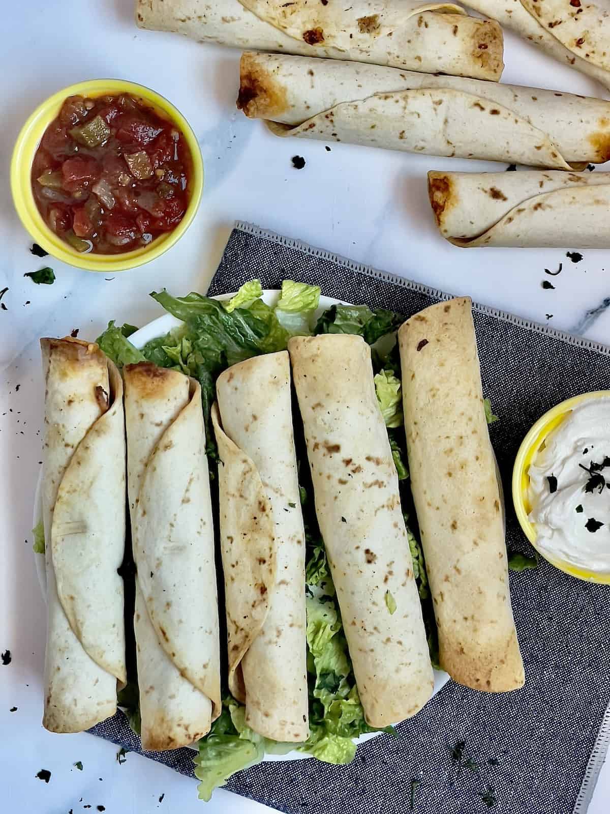 air fryer taquitos on a napkin with guacamole, salsa, and sour cream