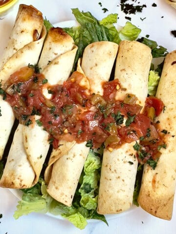 air fried taquitos on a plate of lettuce and topped with salsa and cilantro