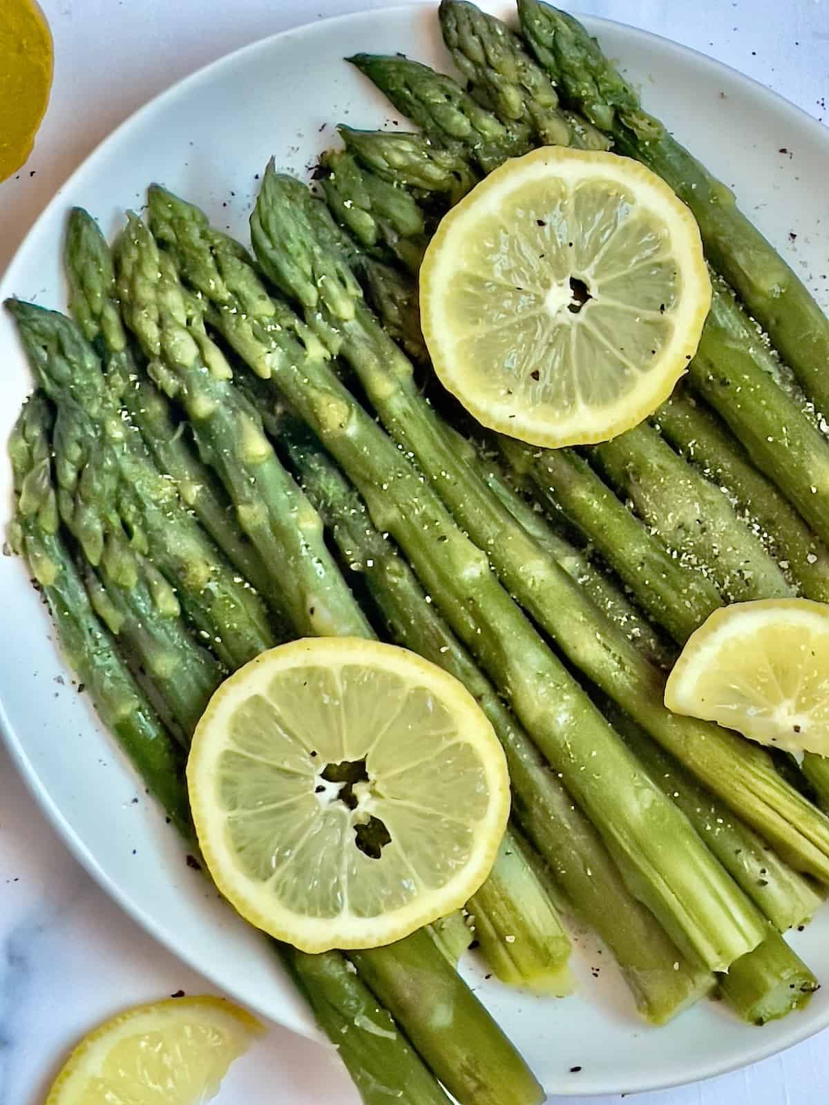 pressure cooked asparagus spears on a plate topped with lemon slices