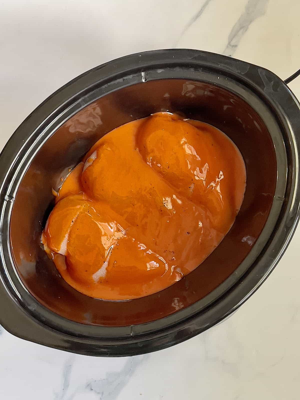 chicken breasts topped with buffalo sauce in a slow cooker