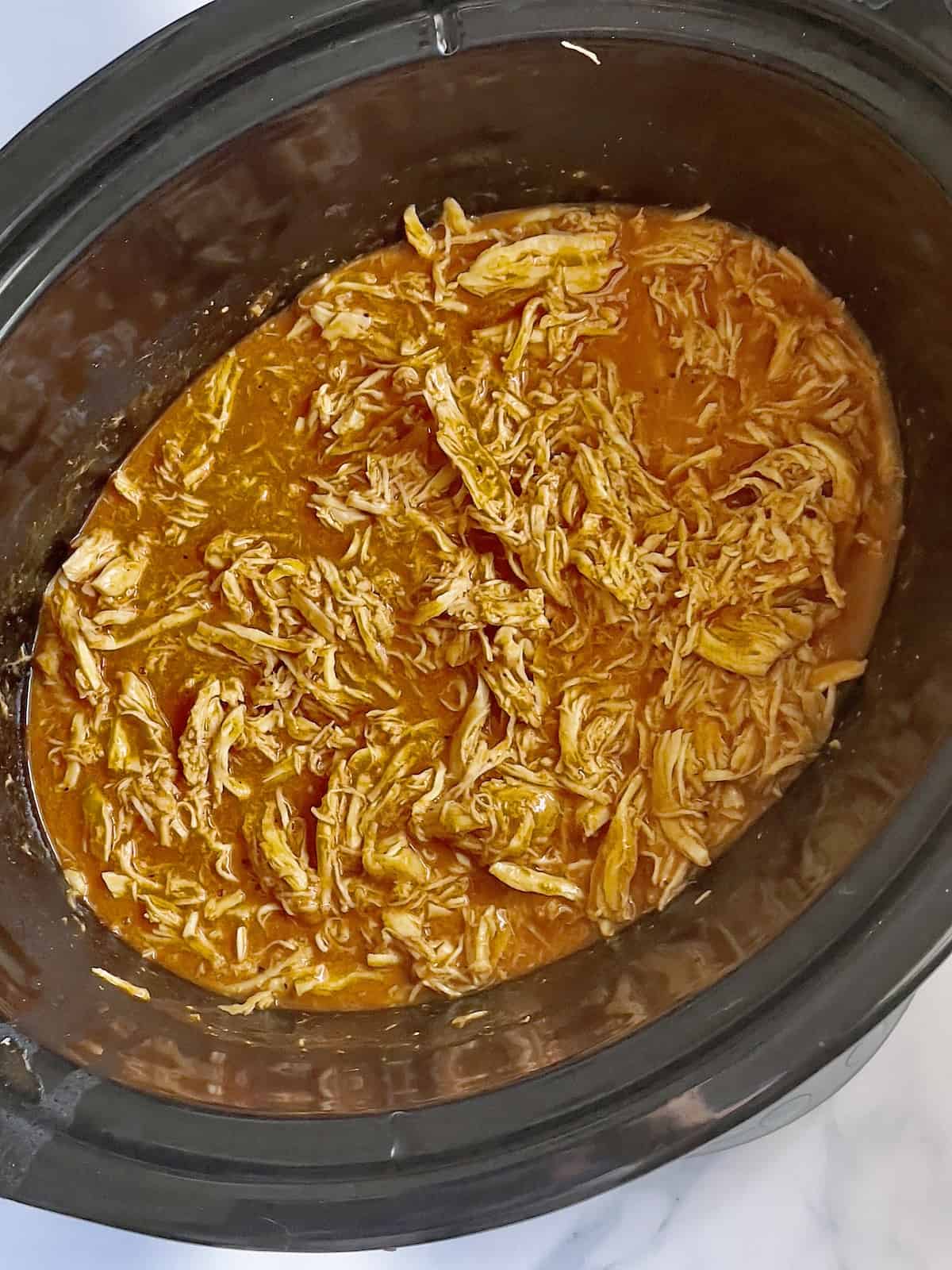 shredded buffalo chicken in hot sauce in a slow cooker