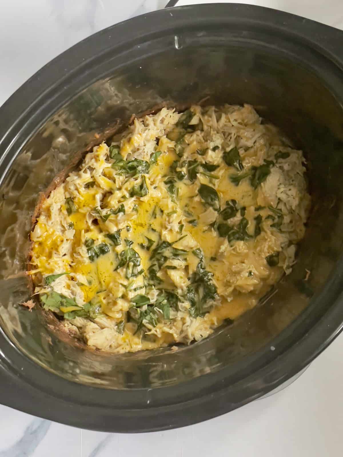 shredded chicken in a crockpot topped with spinach, scallions and cheddar cheese