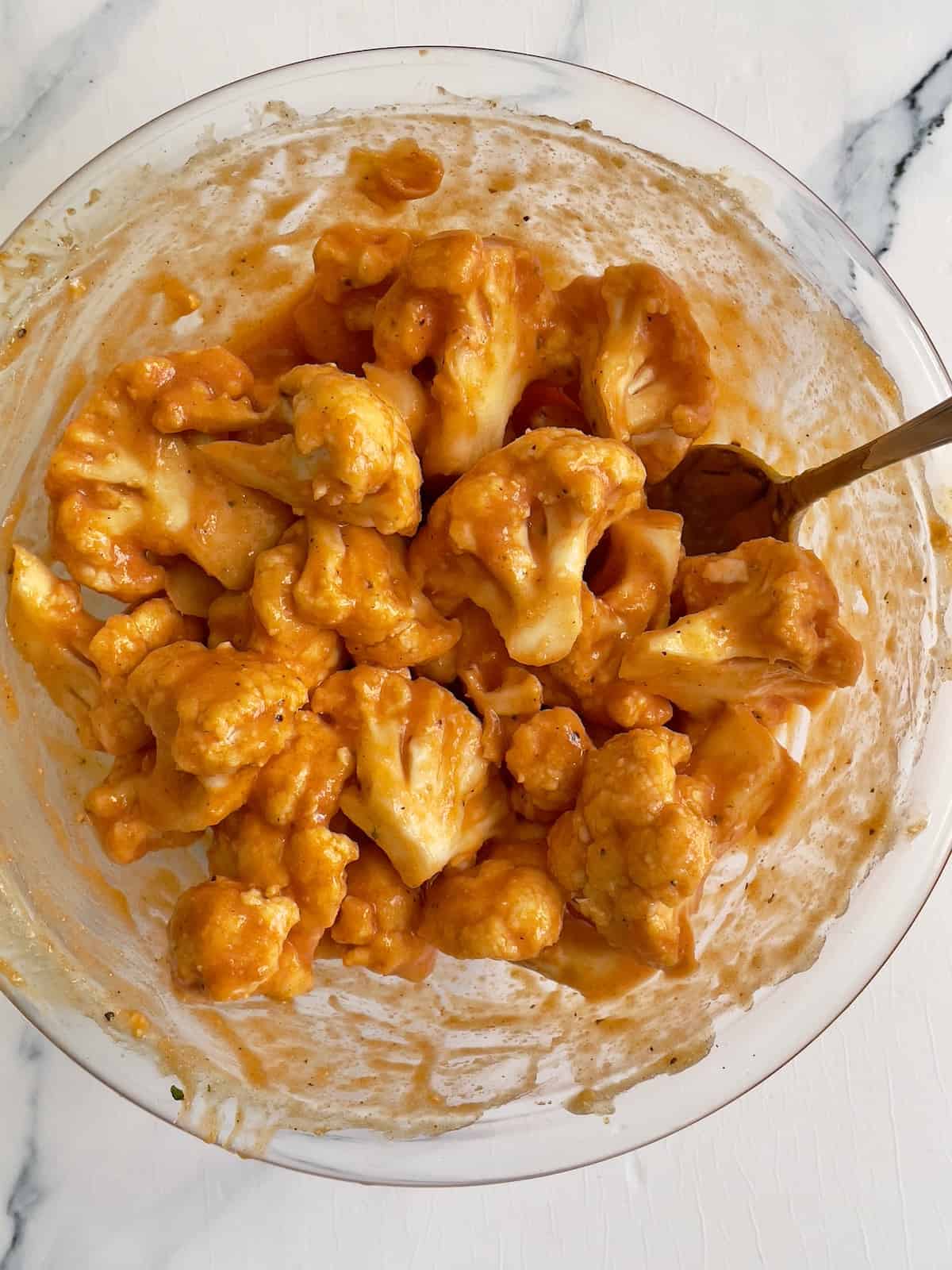 cauliflower florets in a large mixing bowl tossed with buffalo sauce, garlic salt, and pepper