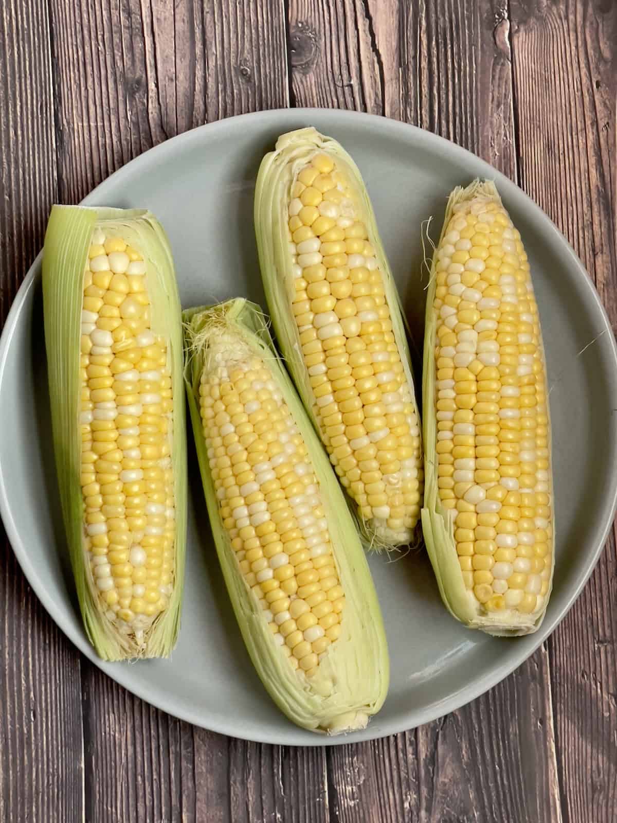 four ears of corn on a gray plate in their husks
