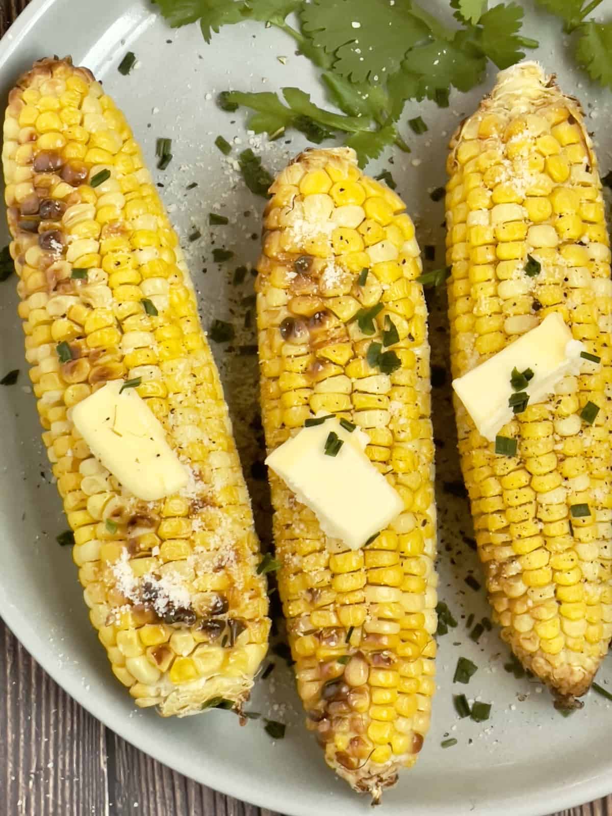 close up of air fryer corn on the cob on a gray plate topped with butter