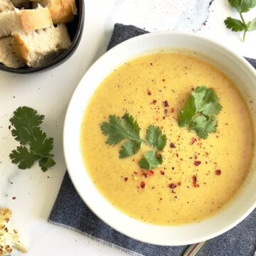 instant pot cauliflower soup in a white bowl topped with parsley leaves and red pepper flakes