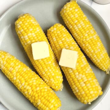 pressure cooked corn on the cob on a gray plate with butter pieces