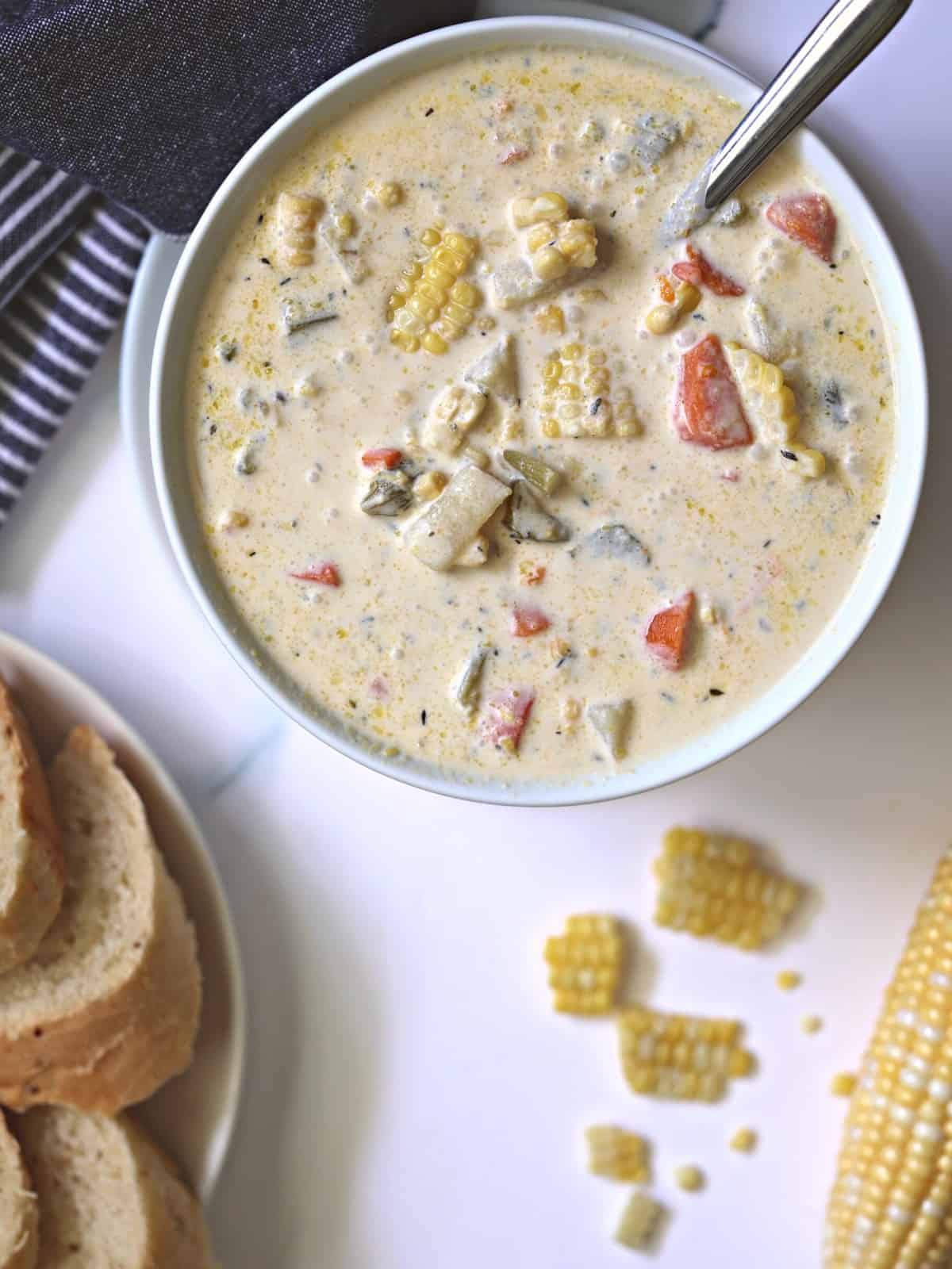 creamy corn chowder in a white bowl with sliced bread and corn kernels