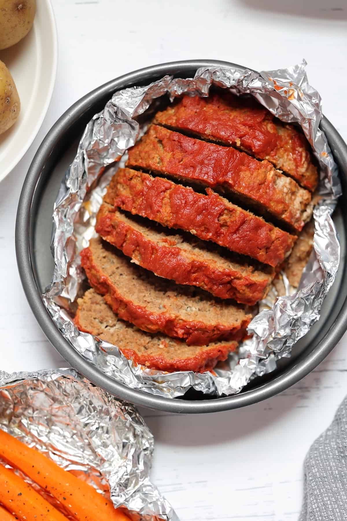 pressure cooker meatloaf in a foil pan with potatoes and carrots