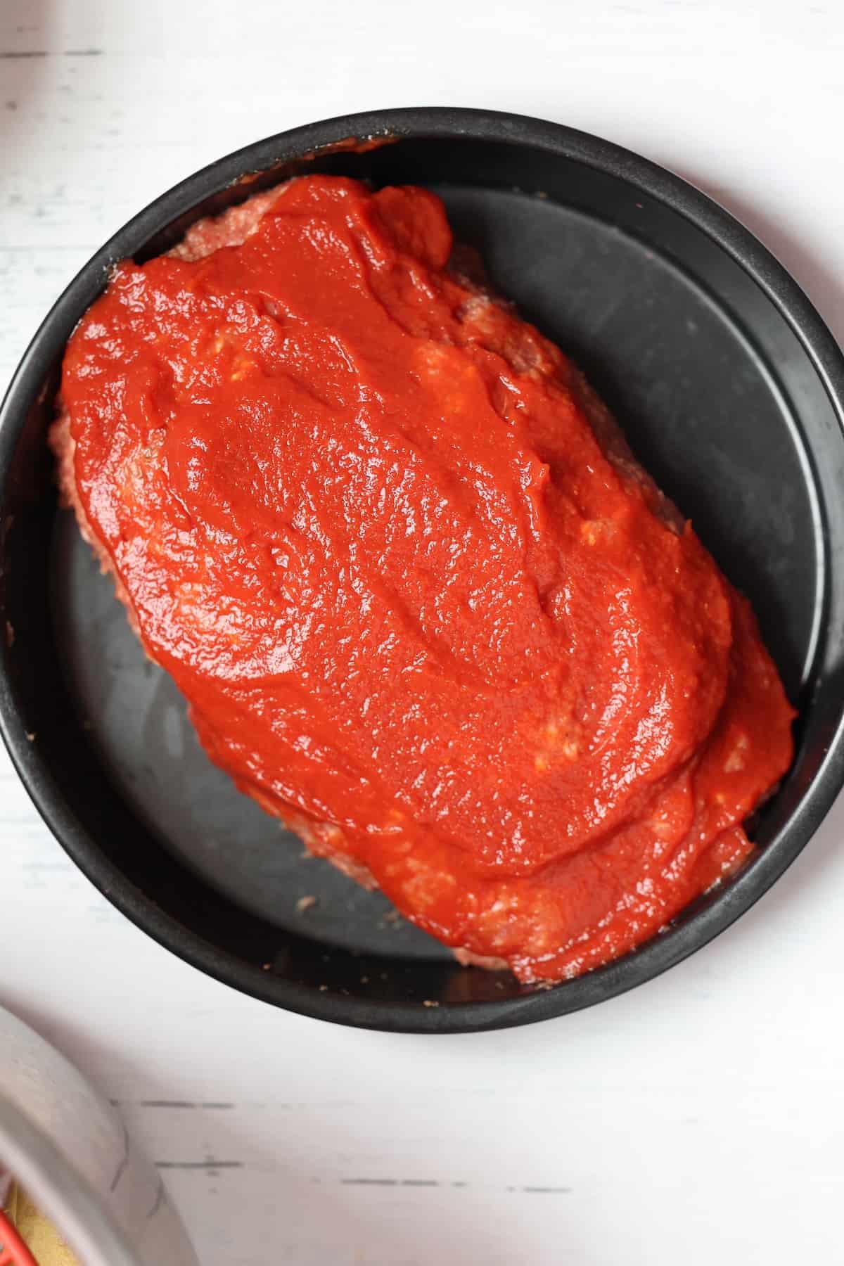 uncooked meatloaf topped with tomato sauce glaze
