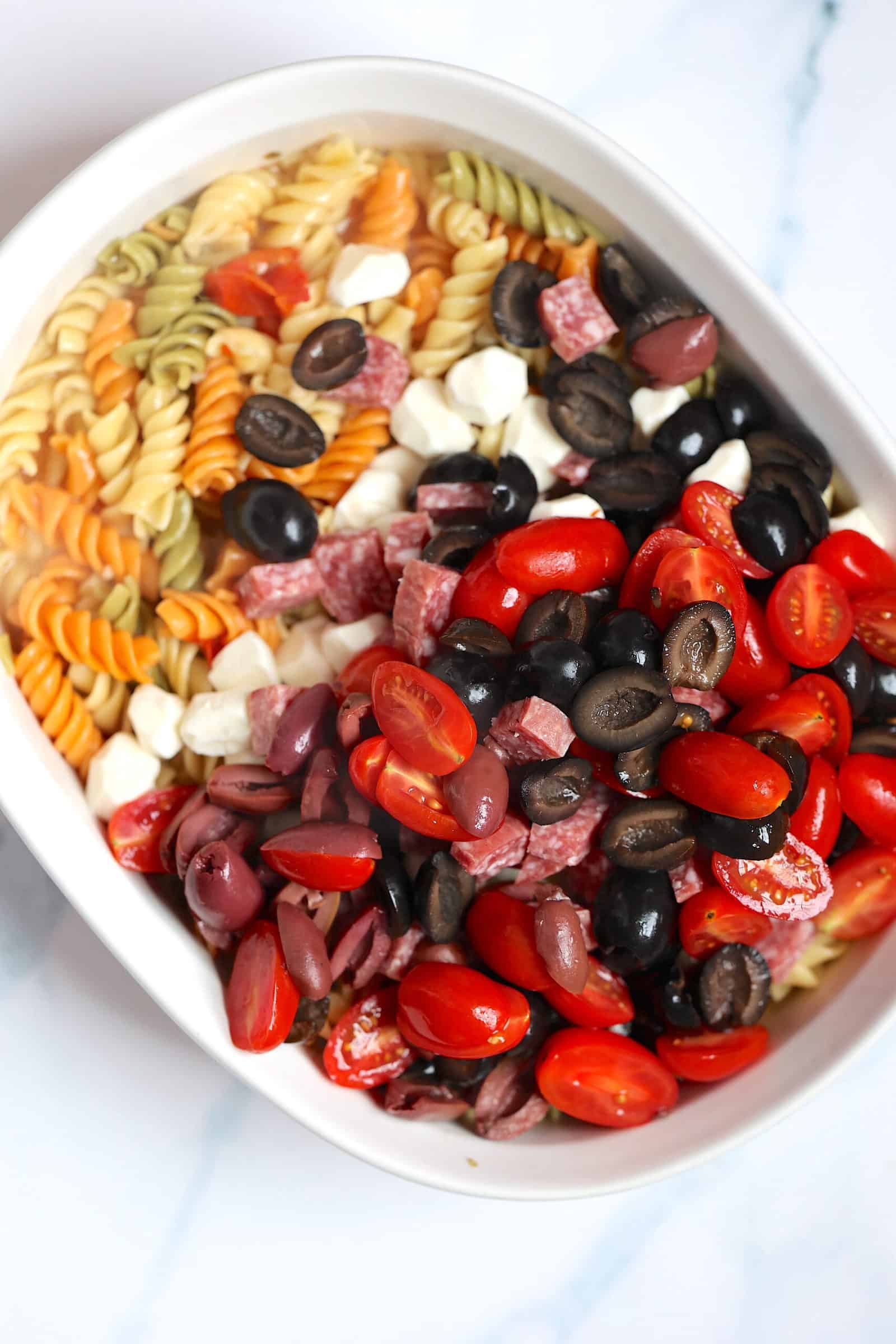 olives, rotini, cheese, and cherry tomatoes in a casserole dish